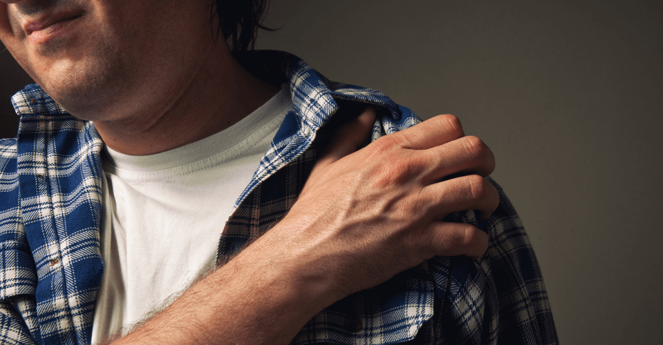 middle aged man with checkered shirt holding shoulder with opposite hand with pain expression