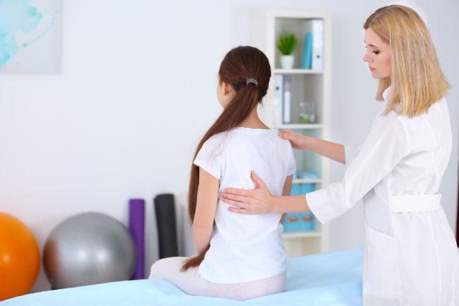 Incorrect posture concept. Physiotherapist examining and correcting girl's back