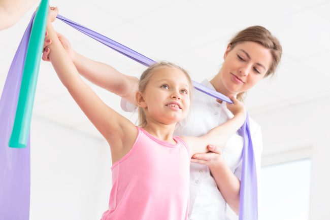 Shot of a little girl doing exercises with a resistance band and assistance of her physiotherapist