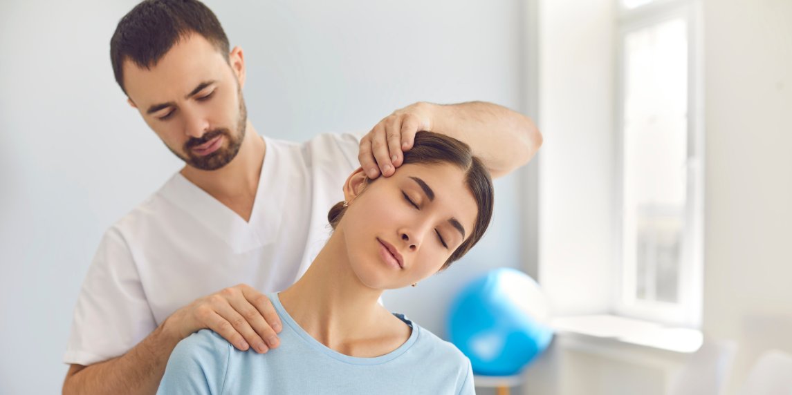 Licensed chiropractor or manual therapist doing neck stretch massage to relaxed female patient in clinic office. Young woman with whiplash or rheumatological problem getting professional doctor's help