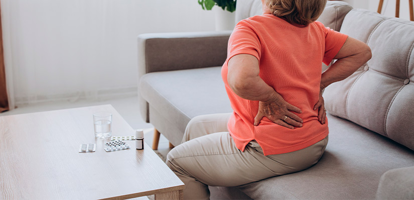 A woman on a couch, showing signs of back pain, reflecting the challenges of managing chronic pain in Texas's hot climate.