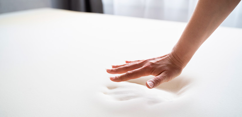 A person gently touching the top of a mattress, illustrating tips for alleviating lower back pain during sleep.