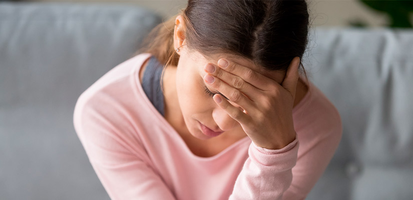  A woman on a couch, hands on her head, expressing distress while undergoing treatment for vertigo.
