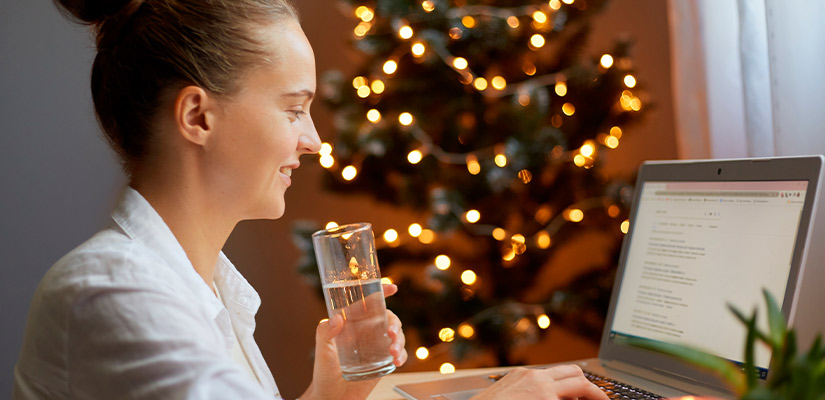 A woman at a desk with a laptop and a glass of water, emphasizing fall hydration and pain relief strategies.