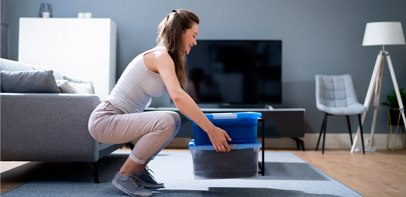 A woman kneels on the floor next to a trash can, focusing on holiday preparations and injury prevention.