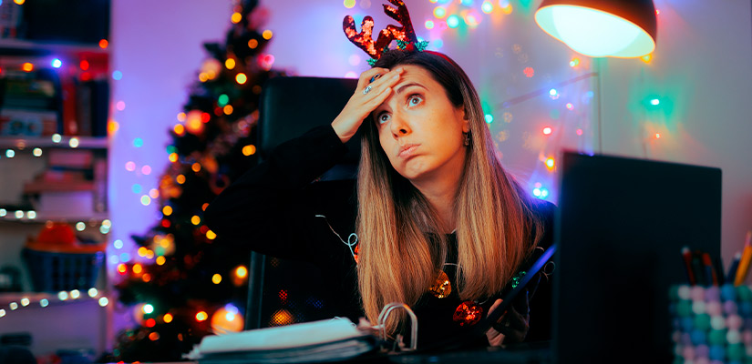 A woman working at a desk with a laptop, illuminated by colorful Christmas lights, symbolizing holiday stress relief.