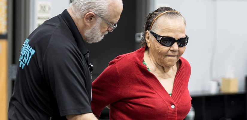 An older man supports an older woman in vestibular physical therapy, promoting her balance and mobility.