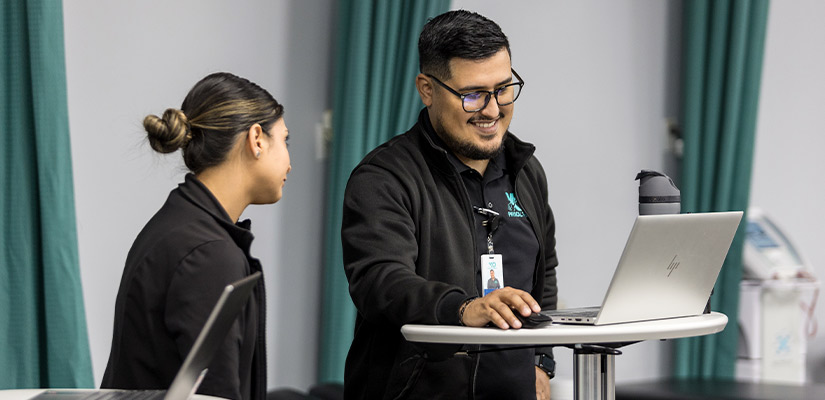 Two professionals collaborating on laptops in an office, related to vestibular physical therapy tasks.