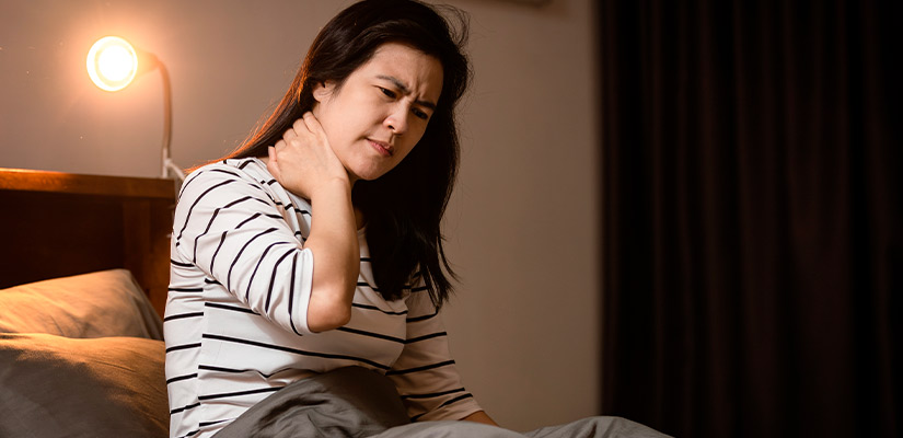 A woman in bed, visibly uncomfortable, is holding her throat, indicating a sore throat.