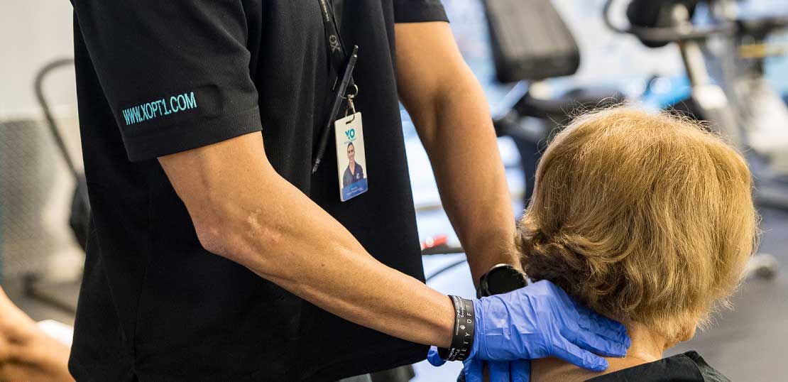 An XO physician assesses a man's neck for any medical concerns in a doctor's office.