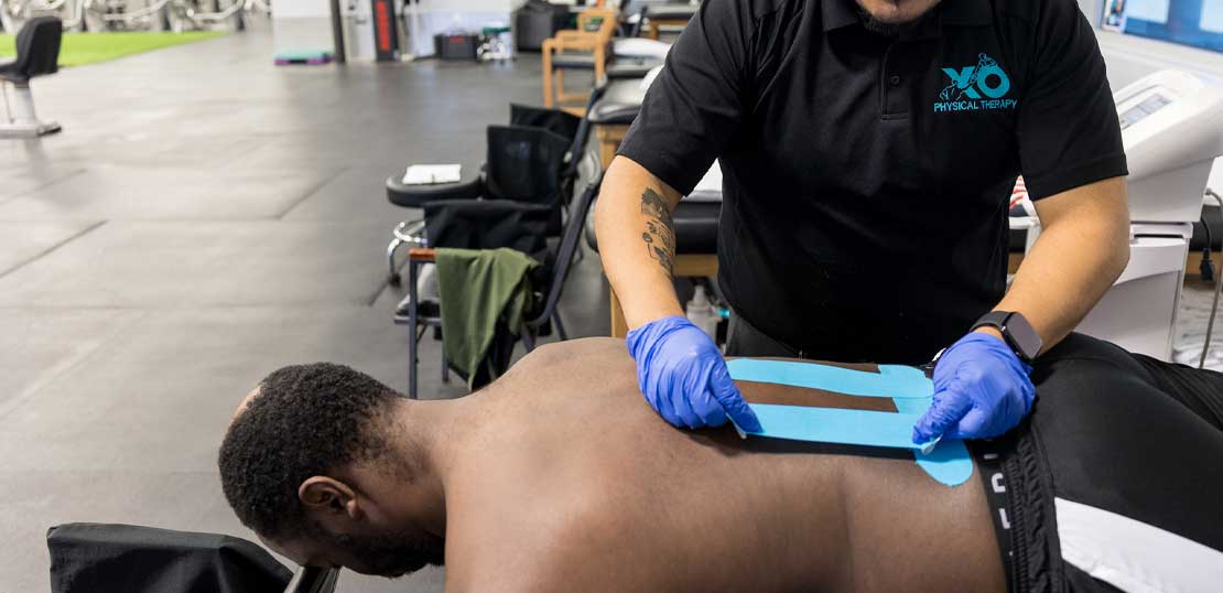  A lies on a massage table receiving rock tape therapy for an XO expert