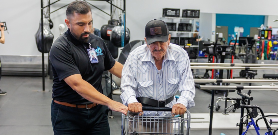 XO Esteban Reyes: Physical therapist assists an elderly man in a wheelchair, demonstrating support and care in a therapeutic setting.